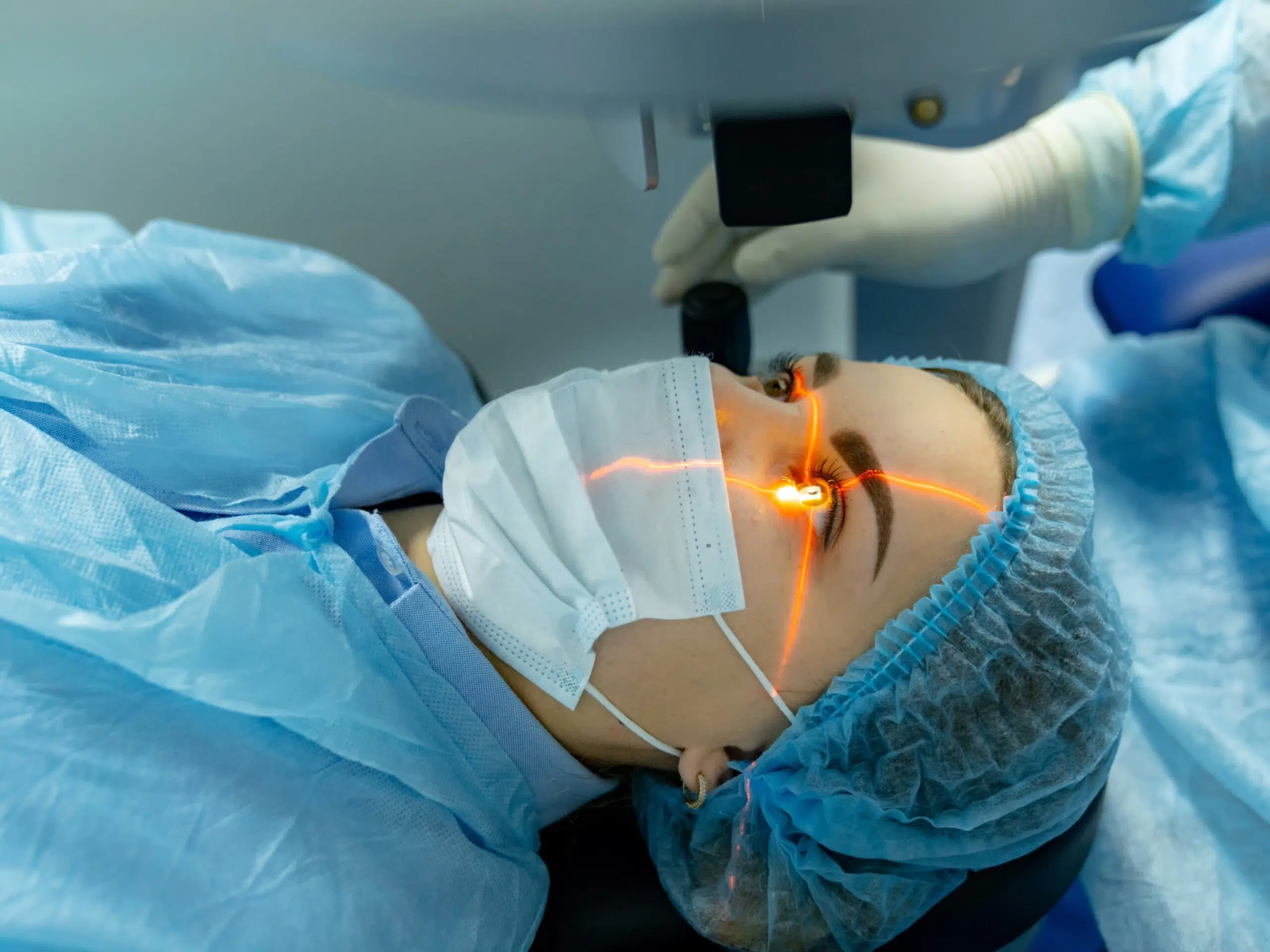 Femme allongée sur une table d'opération avec un faisceau laser orange dirigé vers son œil - Lasik | Pôle Ophtalmologie normandie - Barentin